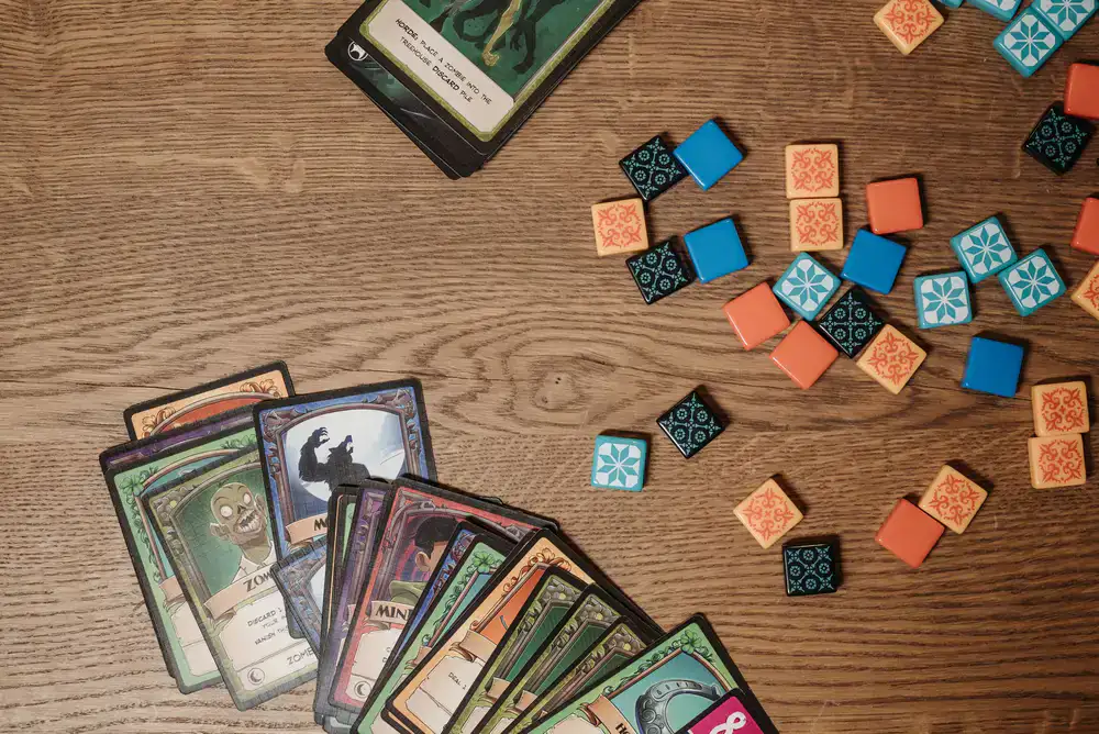 Top-down view of prototype board game components, dice, and cards scattered on a wooden table
